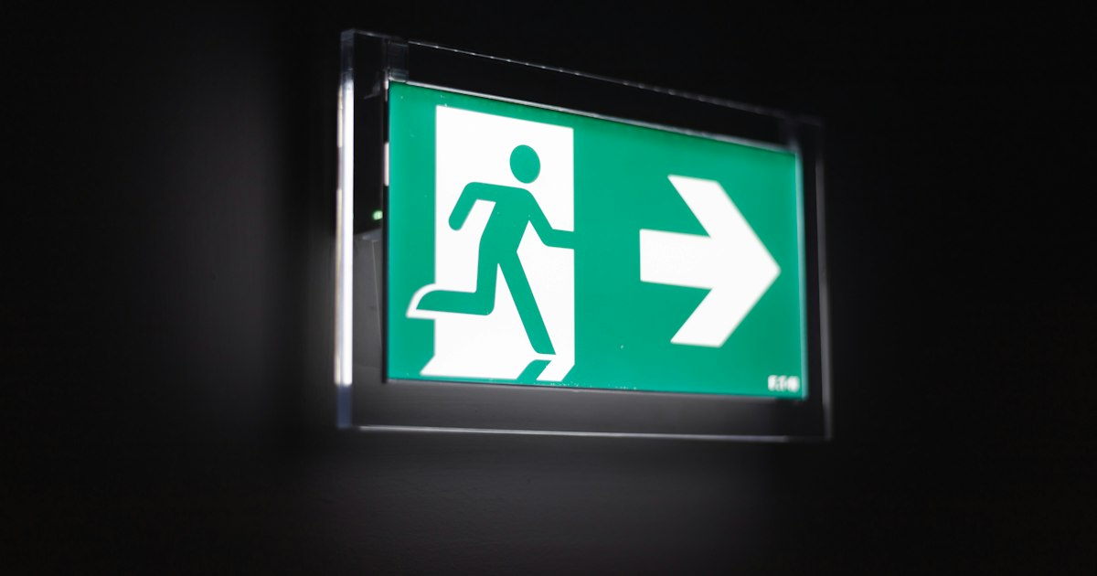 Illuminated green emergency exit sign with a running figure and an arrow on a dark wall